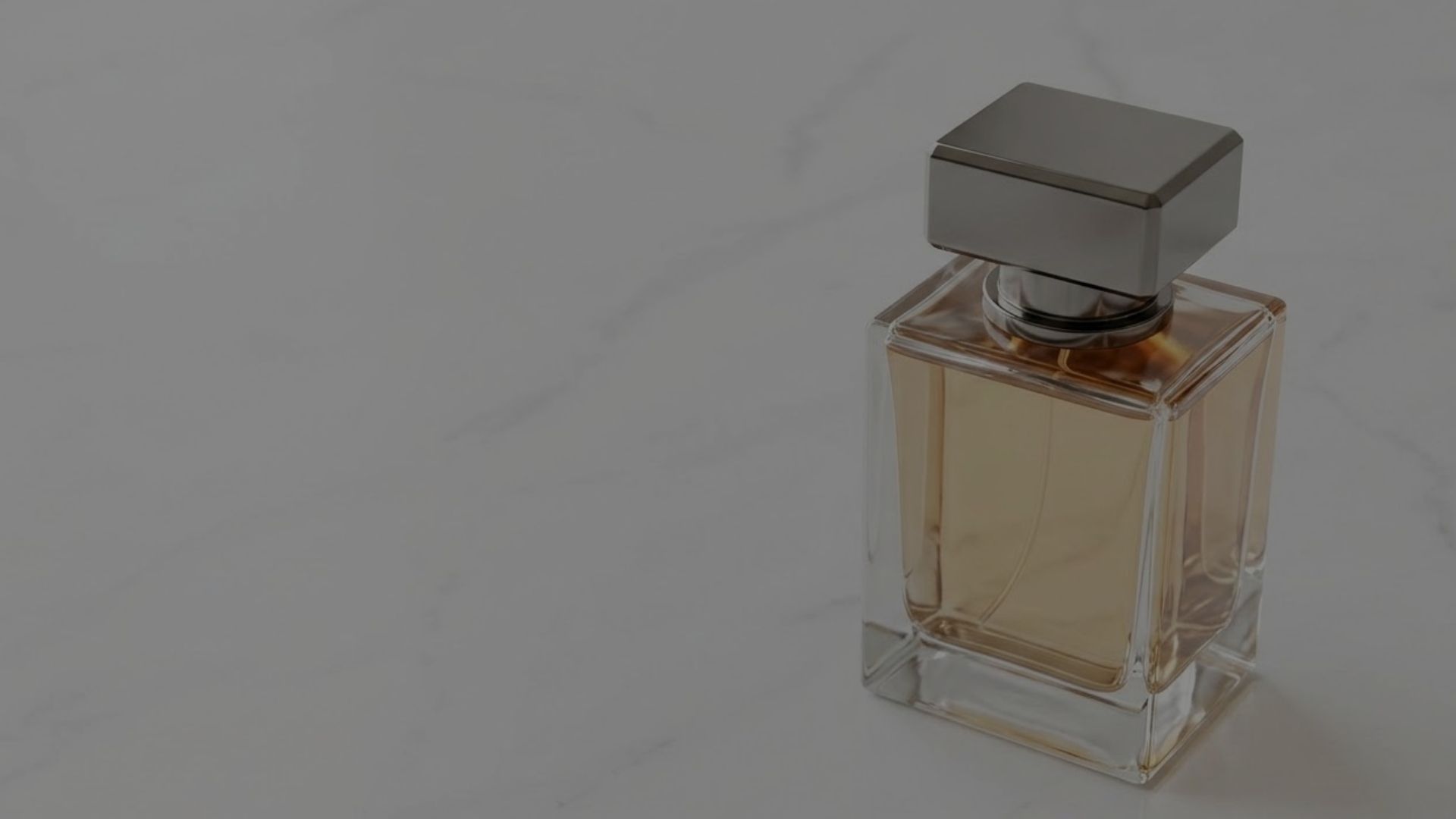 A luxury perfume bottle with a weighted metallic cap sits elegantly on a sunlit marble surface.