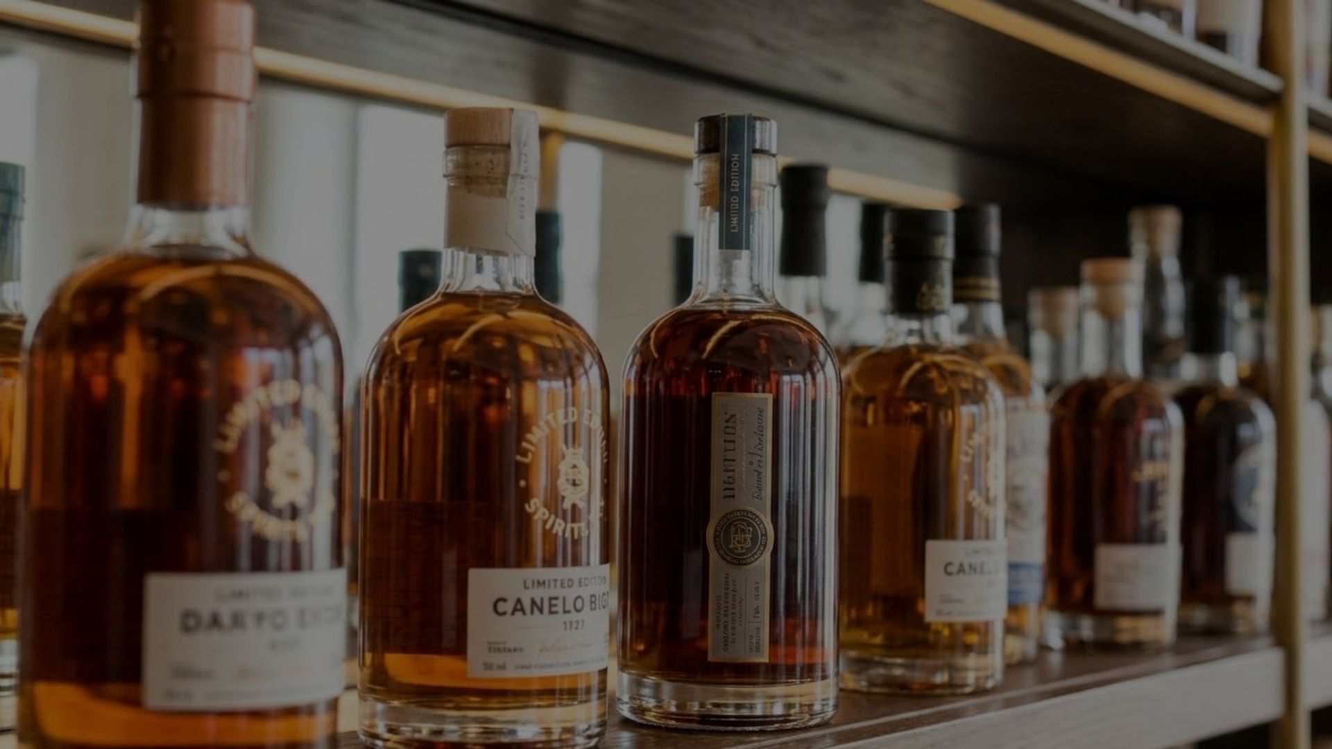 A row of distinctive, premium spirit bottles with unique glass shapes sits elegantly on a well-lit high-end bar shelf, ready to capture attention.