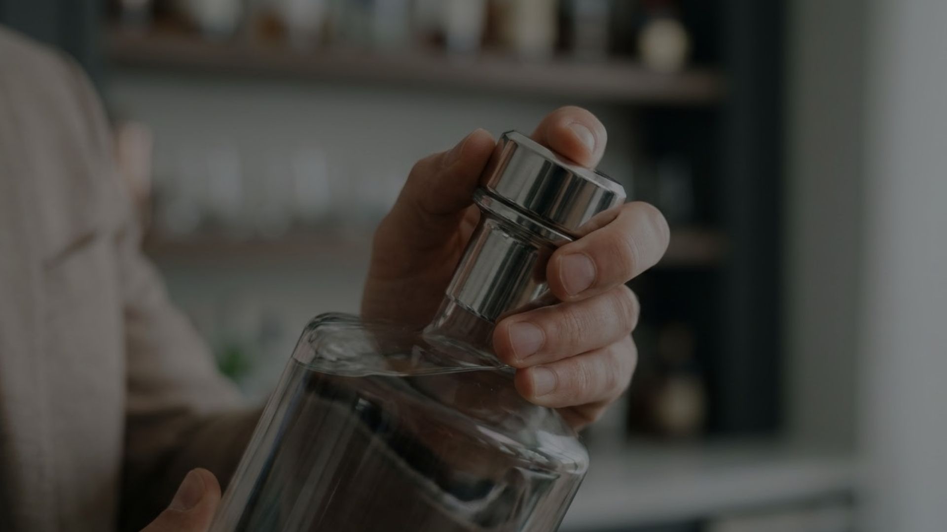 A close-up view of a person holding and feeling the heavy, metallic closure of a premium spirit bottle in a sophisticated bar setting.